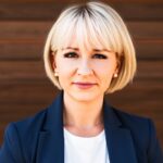 Amery Treble-Barna, PhD, headshot with a brown, wood paneling behind her she is wearing a blue blazer over a white shirt.